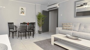 Uma sala de estar moderna com área de jantar, um sofá cinzento, uma mesa de centro e um ventilador de teto.