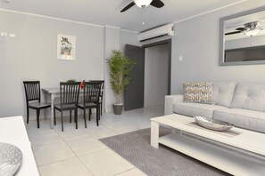 A modern living room with a dining area, a grey sofa, a coffee table, and a ceiling fan. - Modern 1 Bedr Apartment · Stylish Aruba Stay (Noord)