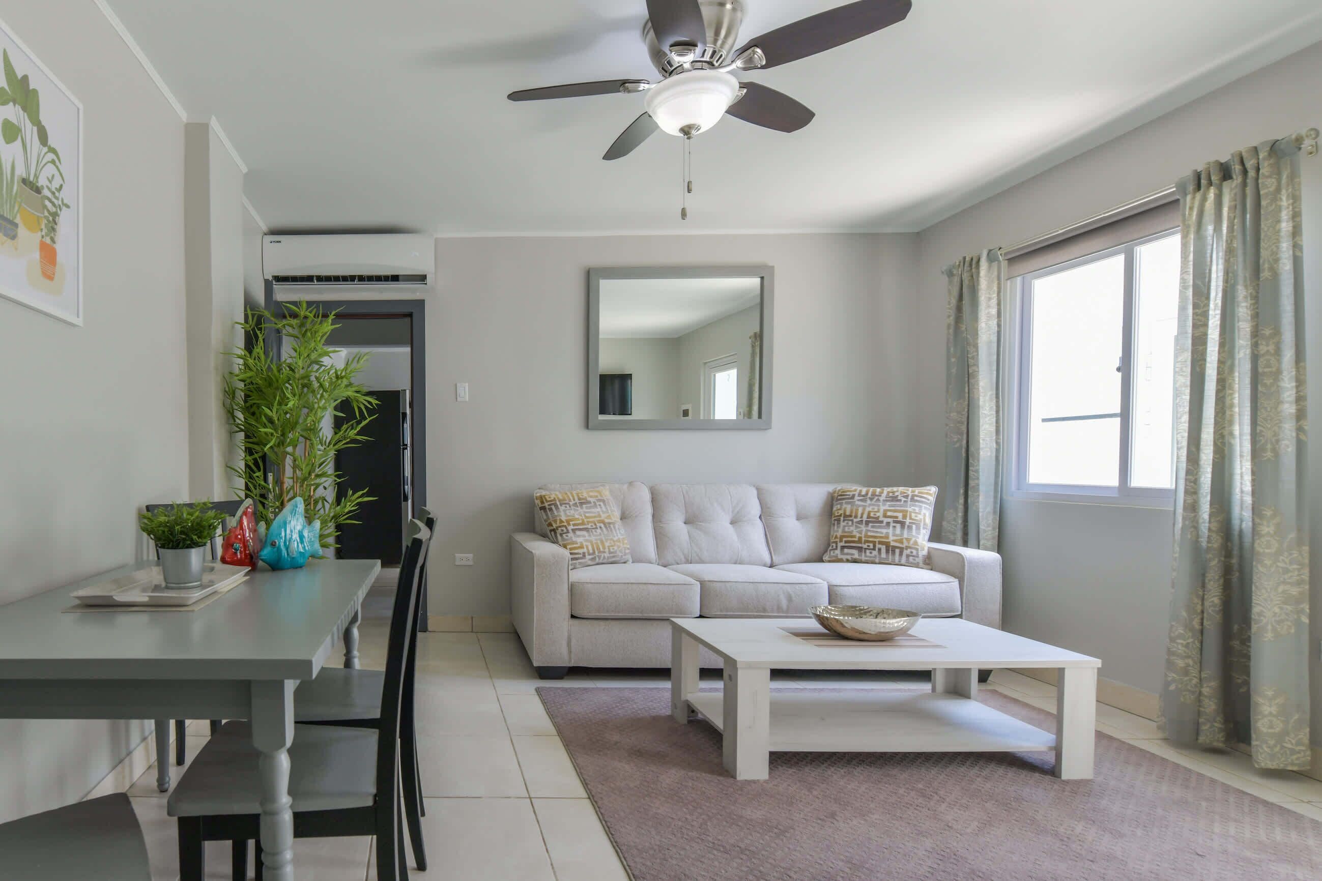 Un salon moderne doté d’un ventilateur de plafond, d’un canapé, d’une table basse et d’un coin repas avec des chaises et une table.