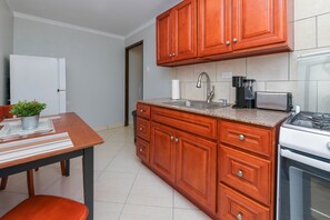 Uma cozinha compacta com armários de madeira, uma pia de aço inoxidável, um fogão e uma cafeteira.