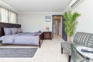 Ein Hotelzimmer mit Bett, Nachttisch, Lampe, Stuhl und einem kleinen Tisch mit Fernbedienung.