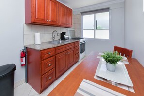 A compact kitchen with wooden cabinets, a stainless steel sink, a stove, and a window providing natural light. - Modern Aruba Studio · Stylish & Newly Fitted (Noord)