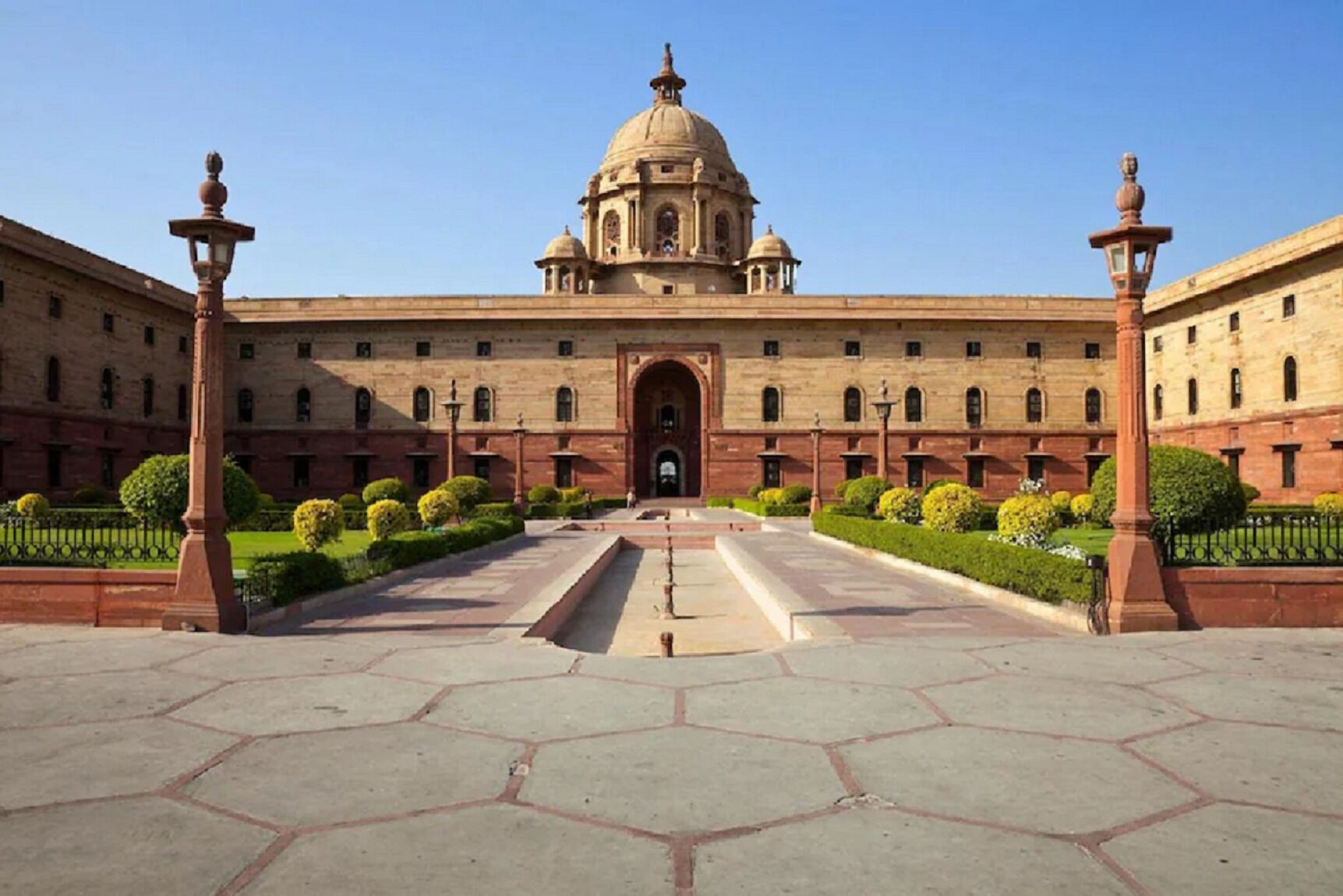 A large building with a central dome and symmetrical wings, featuring a formal entrance and a well-maintained garden.
