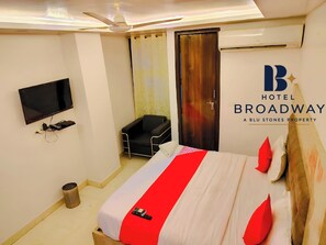 A hotel room with a bed, a television, a ceiling fan, and an air conditioning unit. - Airport Hotel Broadway (New Delhi)