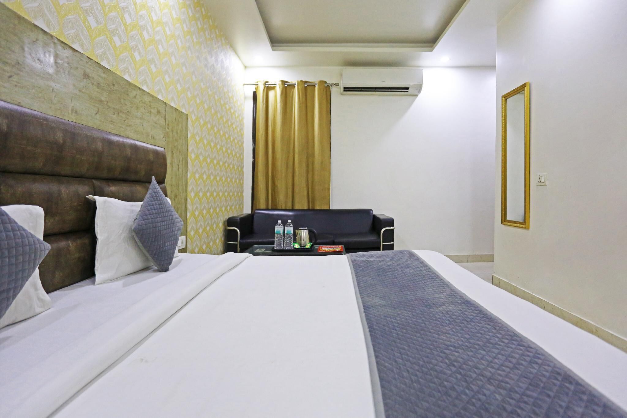 Una habitación de hotel con una cama, un sofá, una mesa de centro con bebidas y un equipo de aire acondicionado.