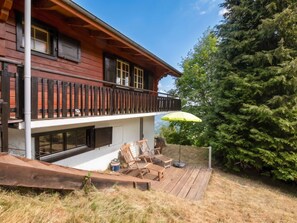 Ein zweistöckiges Holzhaus mit Balkon, Sitzgelegenheit im Freien und einem großen immergrünen Baum.