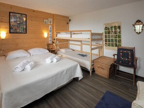 A room with two beds, a wooden bunk bed, a chair, a small table, and a wall with framed pictures. - Prima 1084 by Interhome (Nendaz)