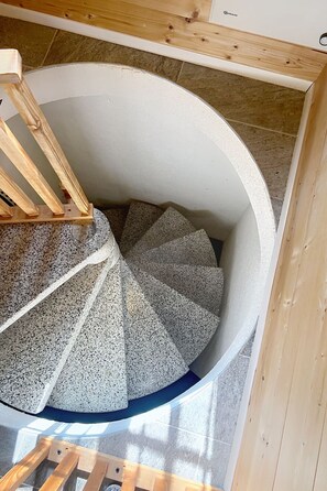 A spiral staircase with a circular design, made of a speckled material, and wooden handrails. - Prima 1084 by Interhome (Nendaz)