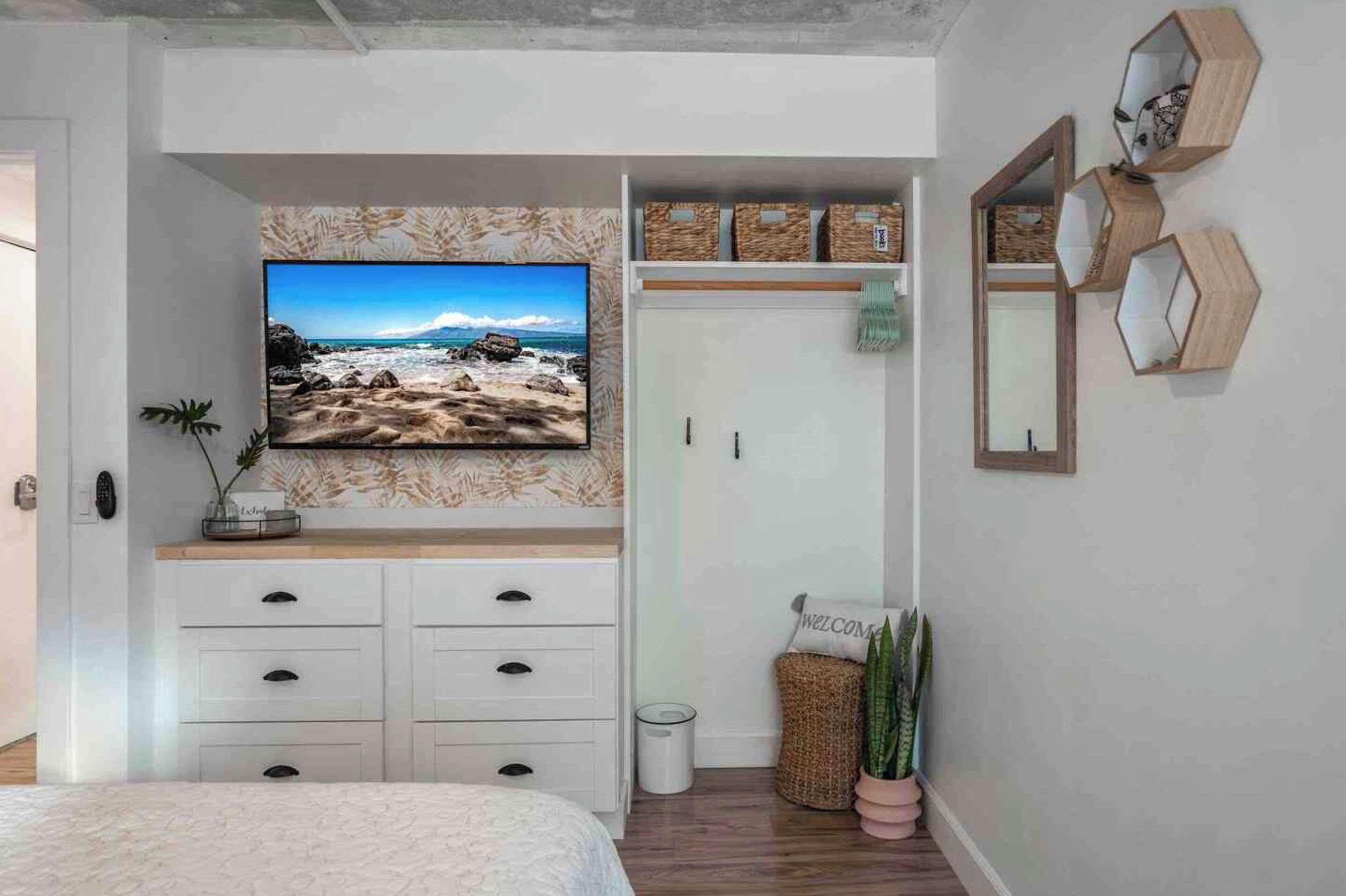 A bedroom with a bed, a television mounted on the wall, a wardrobe, and a small trash bin.