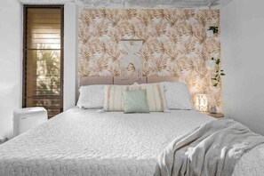 Un dormitorio con cama, mesita de noche, planta en la pared y ventana con persianas.