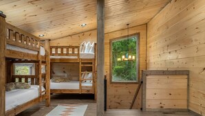A cabin interior with bunk beds, a window with a view of greenery, and a wooden dresser. - 2 Cabin Retreat/Pool/2HotTubs/Playground/Sleeps 22 (Sevierville)
