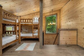 A cabin interior with bunk beds, a window with a view of greenery, and a wooden dresser. - 2 Cabin Retreat/Pool/2HotTubs/Playground/Sleeps 22 (Sevierville)