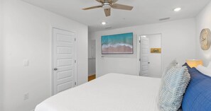 Ein Schlafzimmer mit einem Bett, einem Deckenventilator, einem Gemälde, einer Uhr und einer Tür.