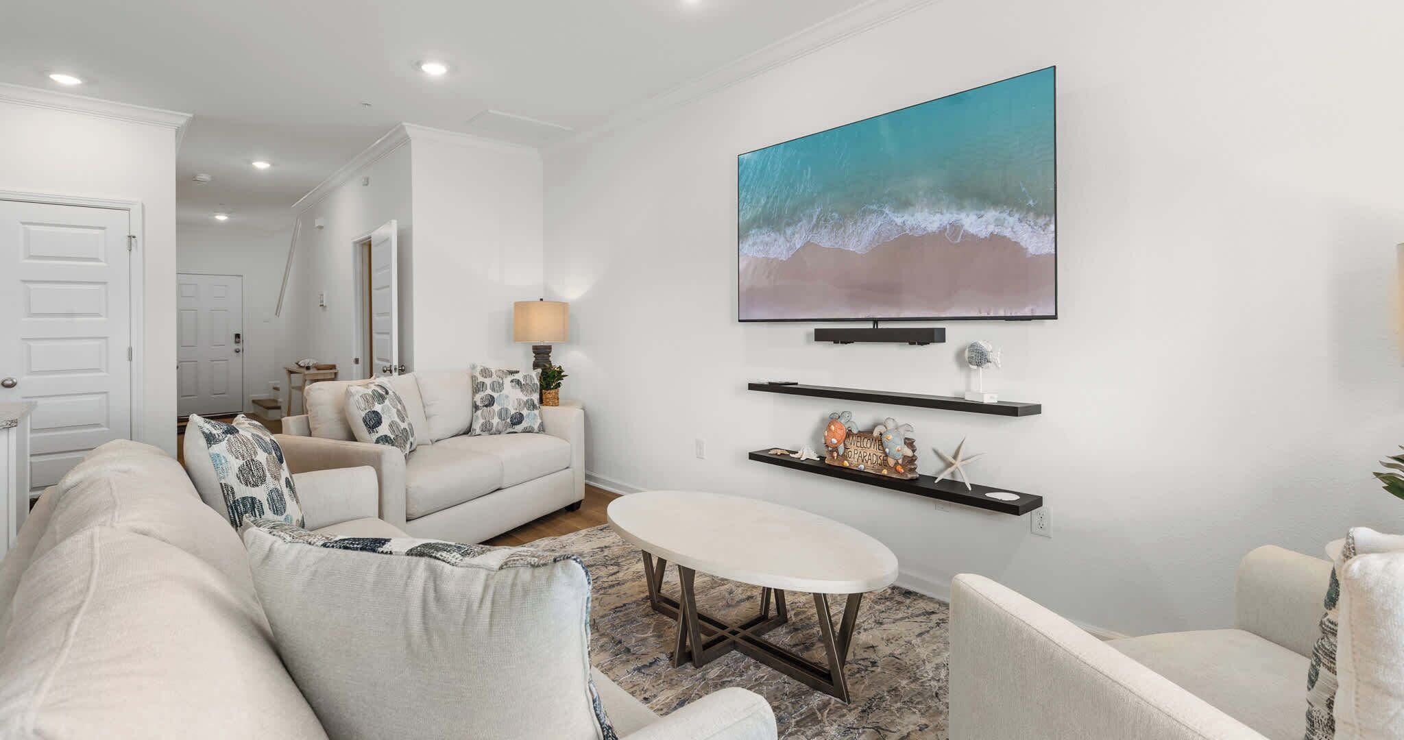 A modern living room with a sofa, armchairs, a coffee table, and a TV mounted on the wall.