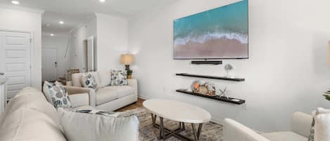 A modern living room with a sofa, armchairs, a coffee table, and a TV mounted on the wall.