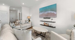 Ein modernes Wohnzimmer mit einer Couch, Sesseln, einem Couchtisch und einem an der Wand befestigten Fernseher.