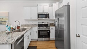 A modern kitchen with white cabinets, stainless steel appliances, and a granite countertop. - Easy Days at Lost Bay - 3BDR (Orange Beach)
