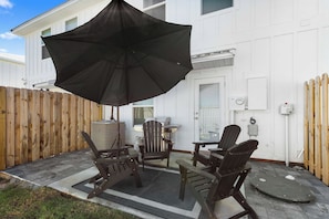 A patio with outdoor furniture, a black umbrella, and a white building in the background. - Easy Days at Lost Bay - 3BDR (Orange Beach)