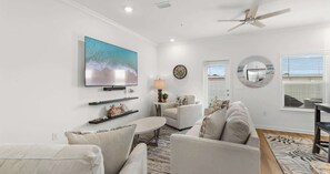 Ein Wohnzimmer mit Flachbildfernseher, Deckenventilator und großem Fenster mit Jalousien.
