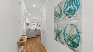 A hallway with a wooden floor leading to a living area with a sofa and a dining table. - Easy Days at Lost Bay - 3BDR (Orange Beach)