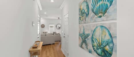 A hallway with a wooden floor leading to a living area with a sofa and a dining table.