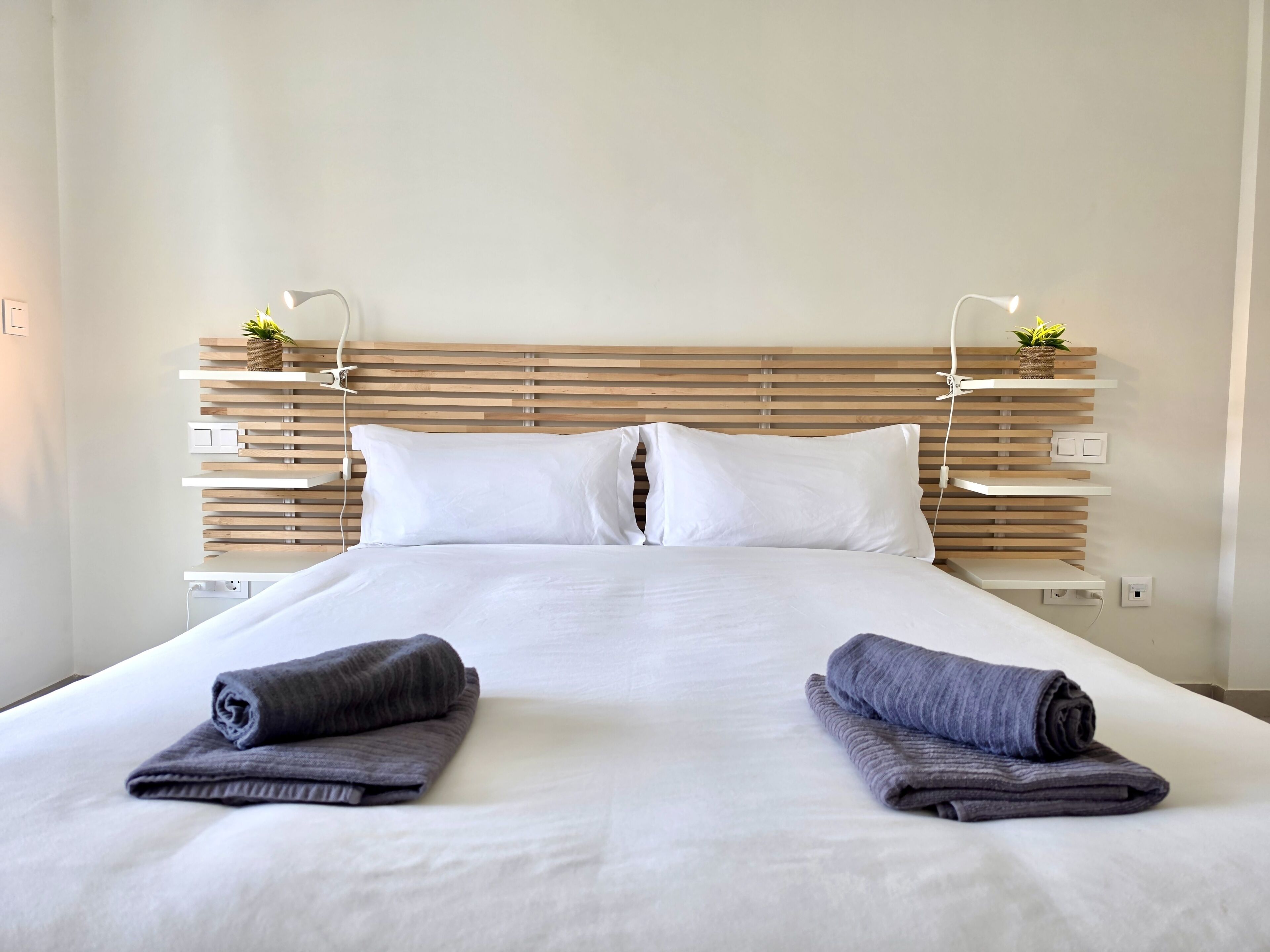 A hotel room with a wooden headboard, white bedding, and two rolled towels on the bed.