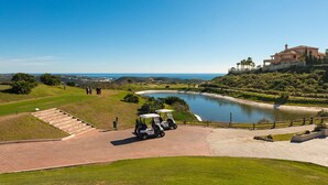 A golf course with a pond, a clubhouse, and a view of the ocean. - SR Calanova Golf and Beach 2-Bedroom Condo in Mijas Costa (Mijas)