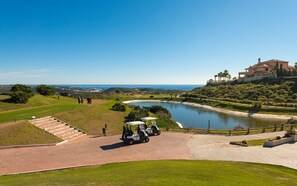 Ein Golfplatz mit Teich, Clubhaus und Blick auf den Ozean.