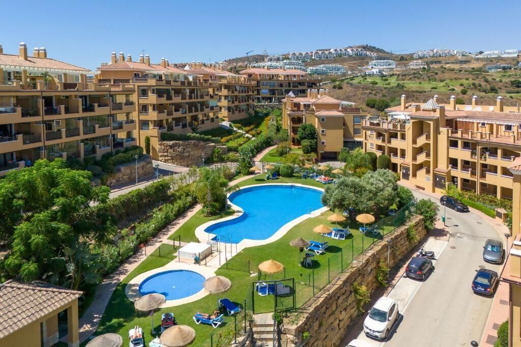 A residential area with a swimming pool surrounded by greenery and a road.