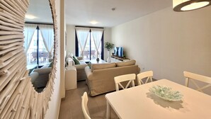 A modern living room with a sofa, a dining table, and a TV. - SR Calanova Golf and Beach 2-Bedroom Condo in Mijas Costa (Mijas)