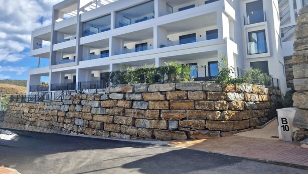 A multi-story building with balconies, a stone retaining wall, and a clear sky. - SR Calanova Golf and Beach 2-Bedroom Condo in Mijas Costa (Mijas)