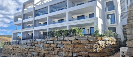 A multi-story building with balconies, a stone retaining wall, and a clear sky.