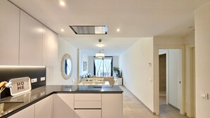 A modern kitchen with a central island, a dining area with a sofa, and a hallway leading to other rooms. - SR Calanova Golf and Beach 2-Bedroom Condo in Mijas Costa (Mijas)