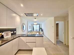 Eine moderne Küche mit einer zentralen Kochinsel, ein Essbereich mit einer Couch und ein Flur zu weiteren Räumen.