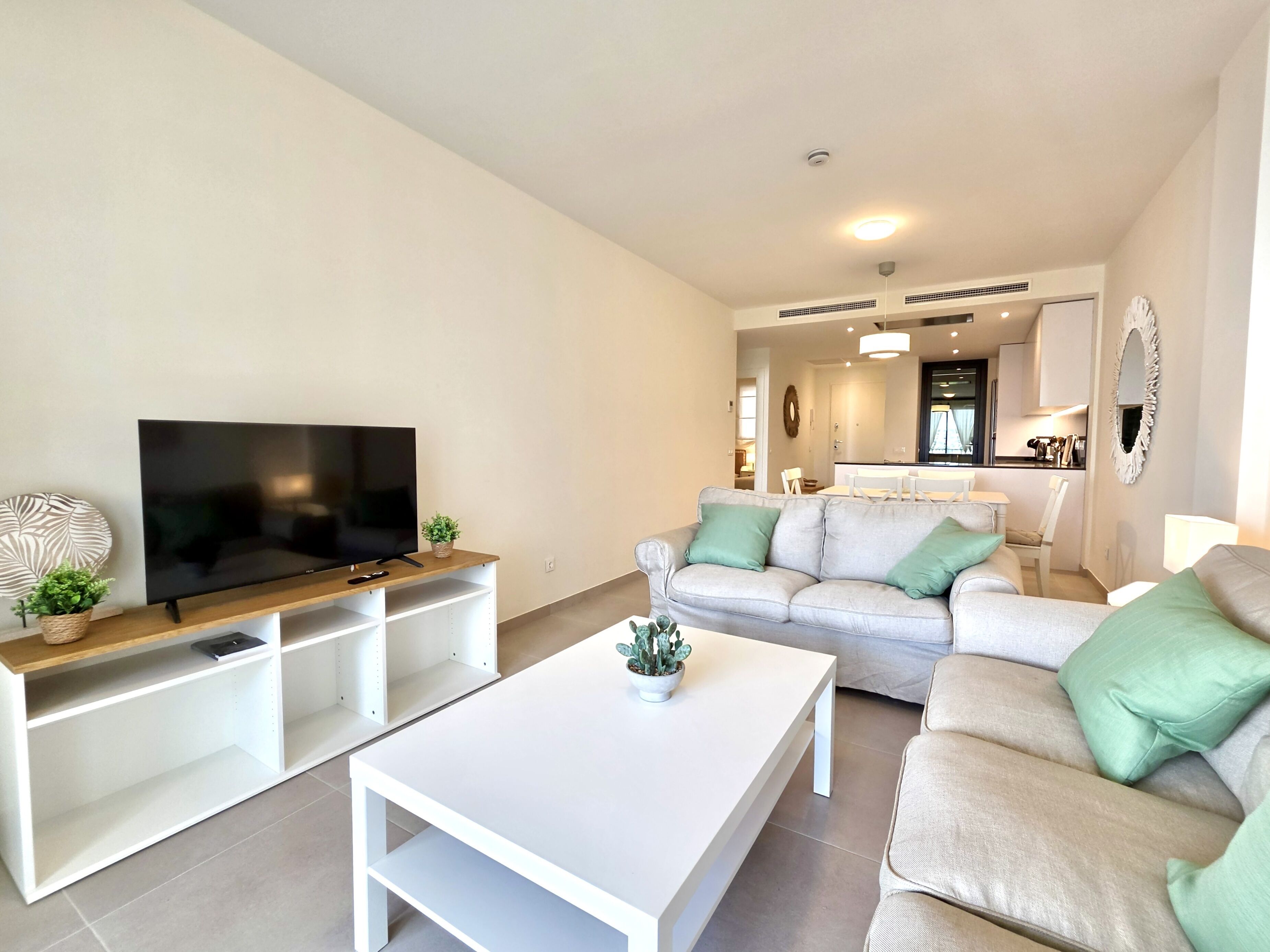 A modern living room with a flat-screen TV, a white coffee table, and two sofas with green cushions.
