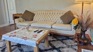 Uma sala de estar com sofá, mesa de centro, abajur e um vaso com flores.