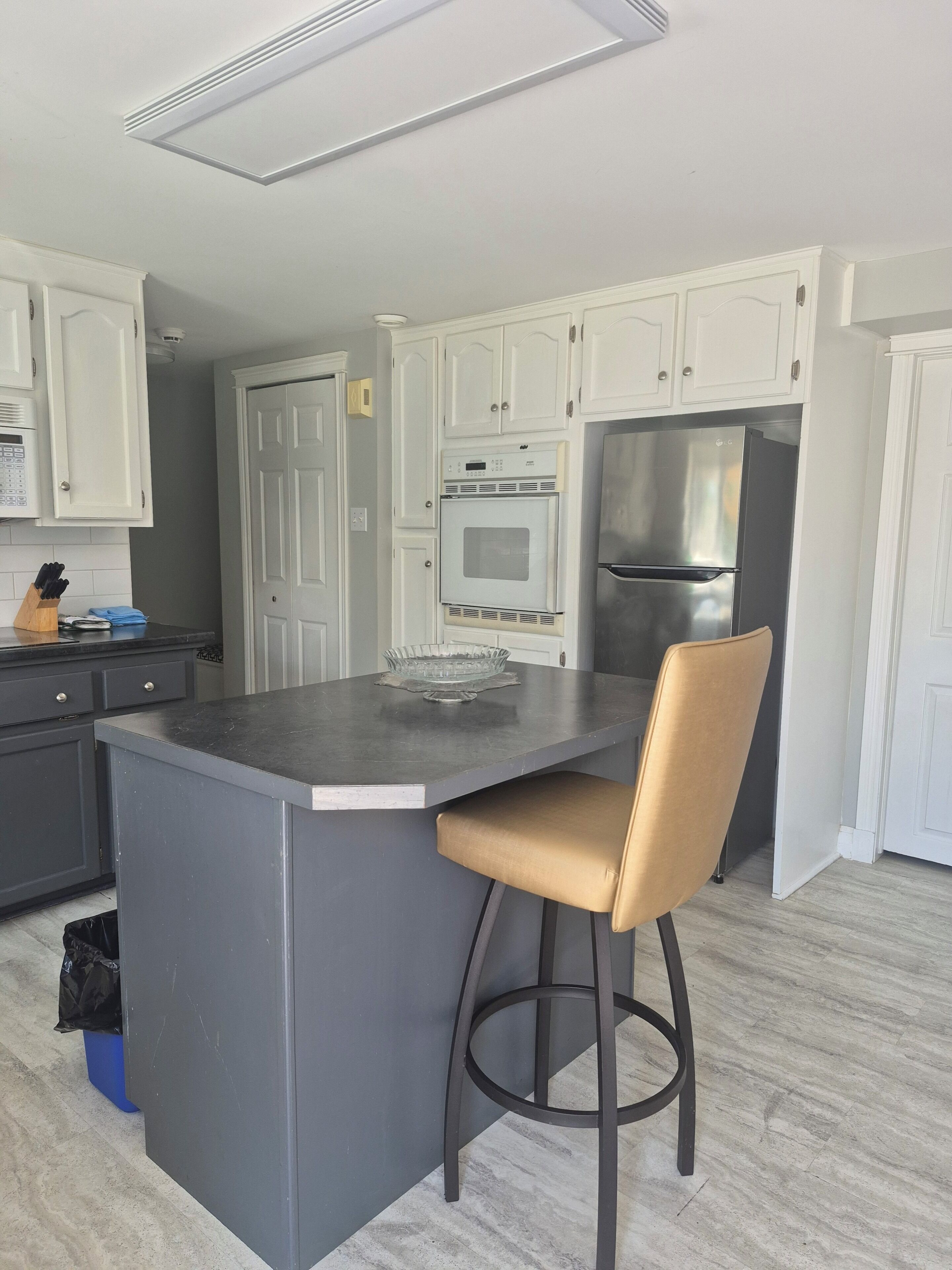A modern kitchen with white cabinetry, a stainless steel refrigerator, and a bar stool.