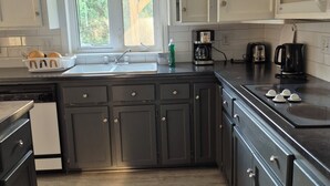 A kitchen with dark cabinets, a white microwave, a coffee maker, and a window with a view of greenery.