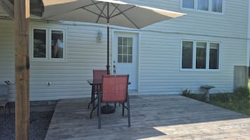 A wooden deck with a table and chairs under a large umbrella, a door, and windows on a house.