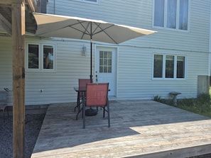 A wooden deck with a table and chairs under a large umbrella, a door, and windows on a house.