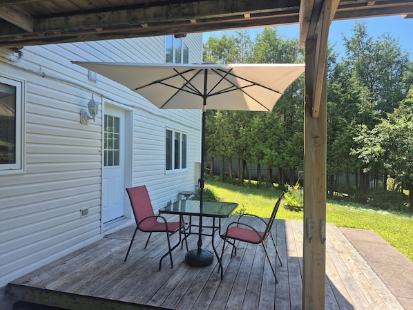 A covered patio with a table and chairs, a large umbrella, and a wooden deck.