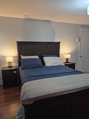 A bedroom with a dark wood headboard, two bedside tables with lamps, a bed with blue bedding, and a white door.