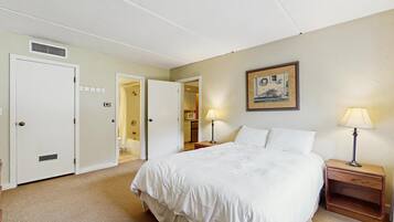 A hotel room with a bed, bedside lamps, a painting on the wall, and a door leading to a bathroom.