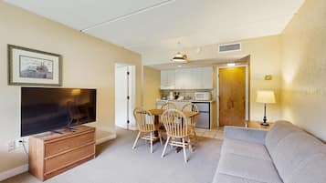 A compact living space with a television, a dining table with chairs, a kitchenette, and a sofa.