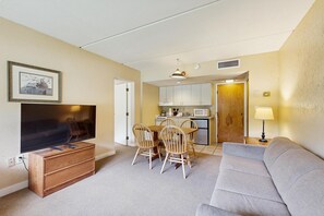 A compact living space with a television, a dining table with chairs, a kitchenette, and a sofa.