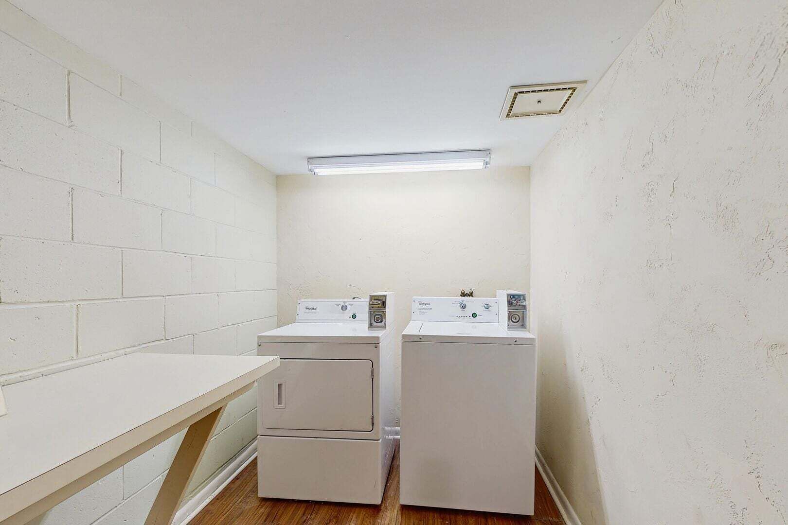 A laundry room with two stacked washers and dryers, a wooden counter, and a fluorescent ceiling light.