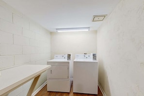 A laundry room with two stacked washers and dryers, a wooden counter, and a fluorescent light.