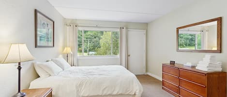 A bedroom with a bed, bedside table, lamp, dresser, mirror, and a window with curtains.