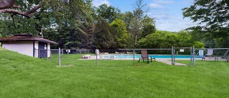 A fenced backyard with a swimming pool, a small shed, and a grassy lawn.
