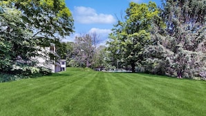 A well-maintained lawn with a small building, surrounded by trees and a clear sky. - Four Season Condo: seasonal pool, ski, hike & golf (Warren)